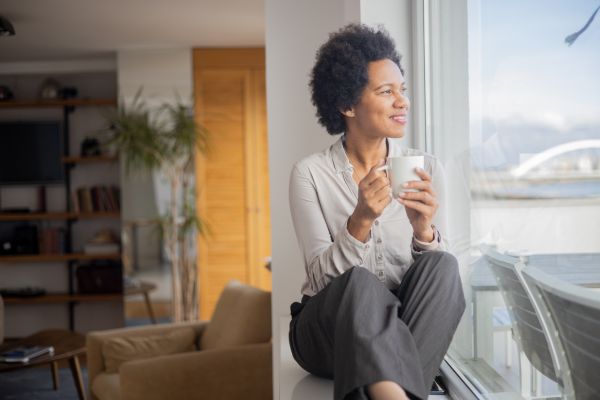 Mujer en menopausia disfrutando de bienestar y paz mental mientras mira por la ventana tomando una taza de café