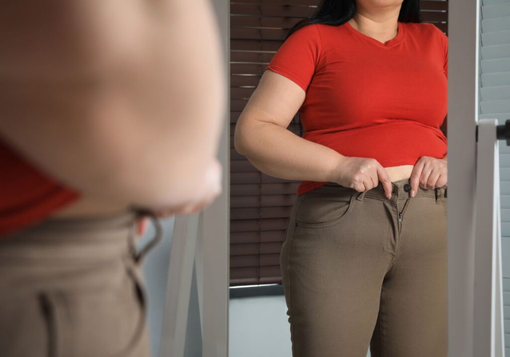 Woman looking at herself in the mirror with discomfort due to body changes