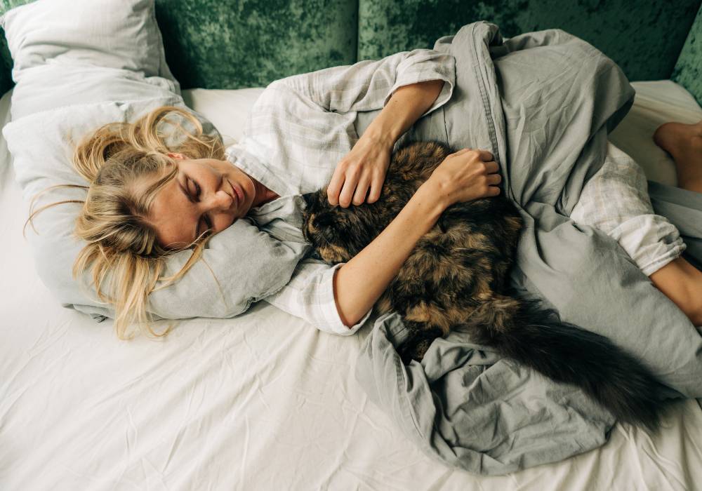 Gato durmiendo junto a su dueña, ejemplo del beneficio de acariciar a tu gato antes de dormir en la menopausia