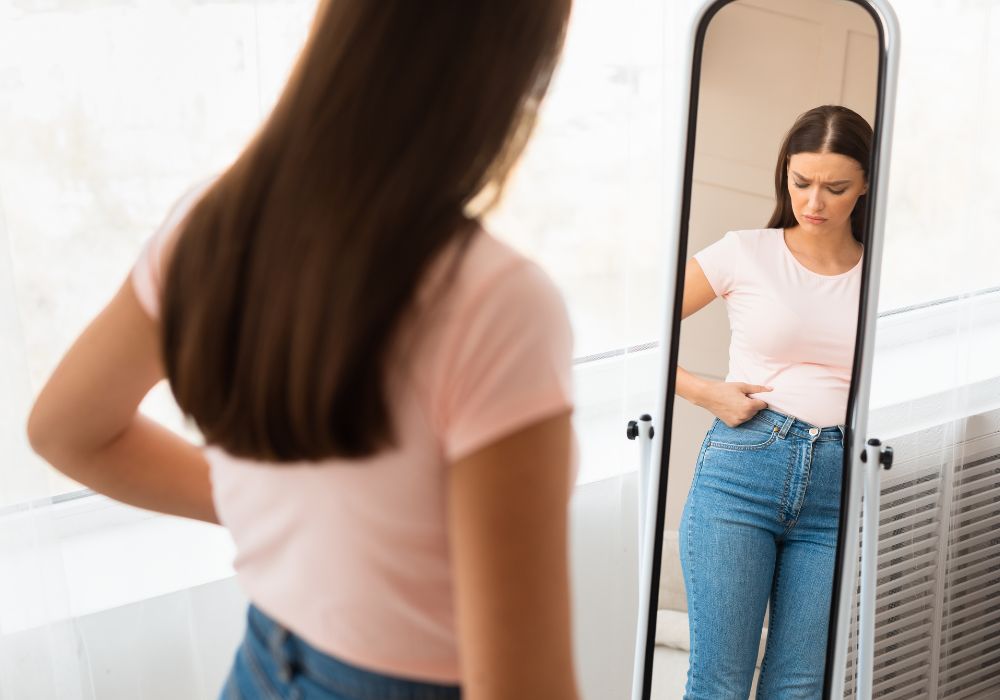 Mujer observando en sí misma la grasa abdominal en la menopausia frente al espejo